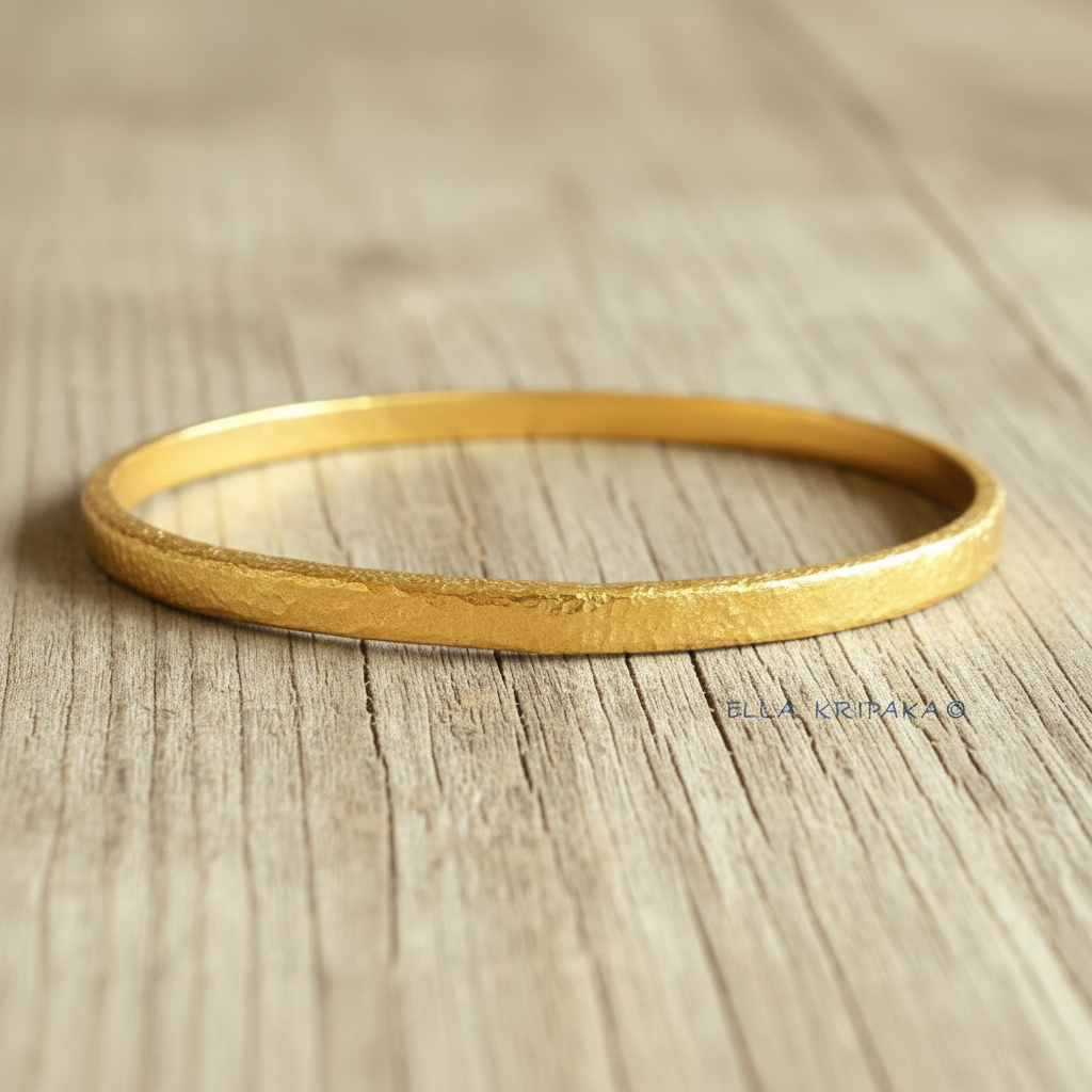 Hammered 24k gold bangle thick textured bracelet on a  light wooden background, branding artist-jeweler name 'Ella Kripaka'