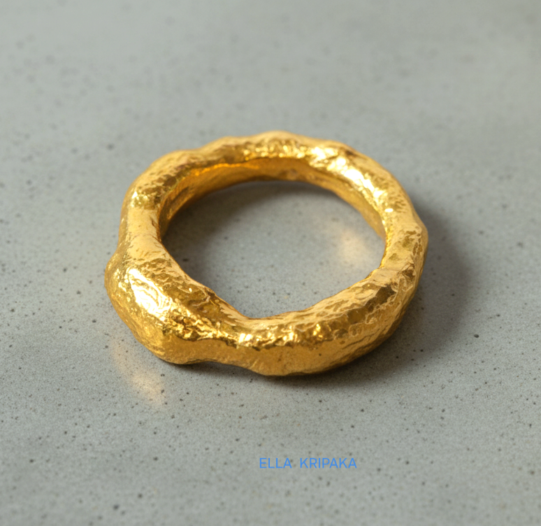 Hammered 24k 9999 Gold thick uneven ring organic signet with a textured gold surface on a grey concrete background, branded 'Ella Kripaka'