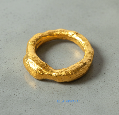 Hammered 24k 9999 Gold thick uneven ring organic signet with a textured gold surface on a grey concrete background, branded 'Ella Kripaka'
