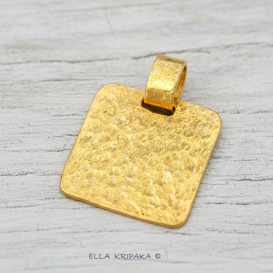 Hammered 24k gold square pendant with shiny forged gold textures on white old wooden surface, artist-jeweler 'Ella Kripaka' branding