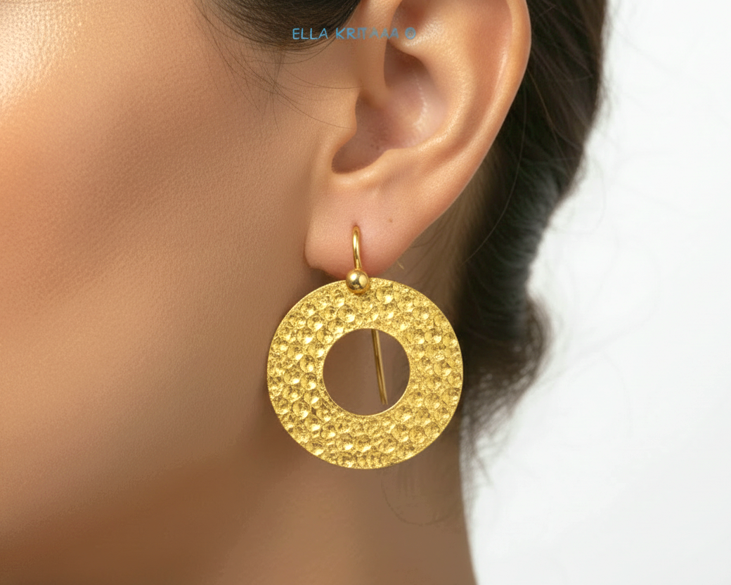 Organic 24k 9999 gold hammered hoop earring with shiny gold textures worn by a model on neutral background, artist-jeweler's name 'Ella Kripaka'