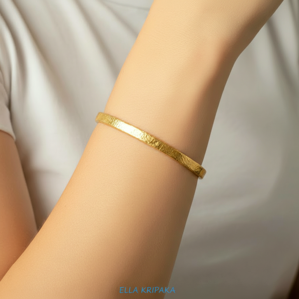 Hammered 24k gold bangle thick bracelet Ancient Rome 34g style worn by a person on hand and on a white t-shirt background, branding artist-jeweler name 'Ella Kripaka'