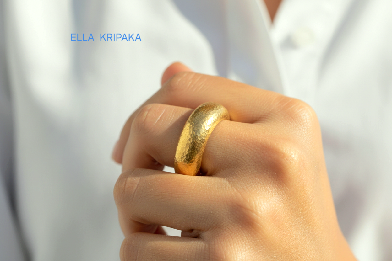 Hammered 24k Gold 9999 gold thick ring band with textured gold worn on model's finger and on a white blurred background, branded 'Ella Kripaka'
