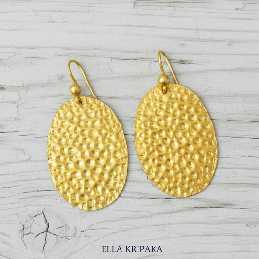 24k gold hammered oval earrings with shiny textured reliefs are on light grey old wooden background, artist-jeweler's name 'Ella Kripaka'