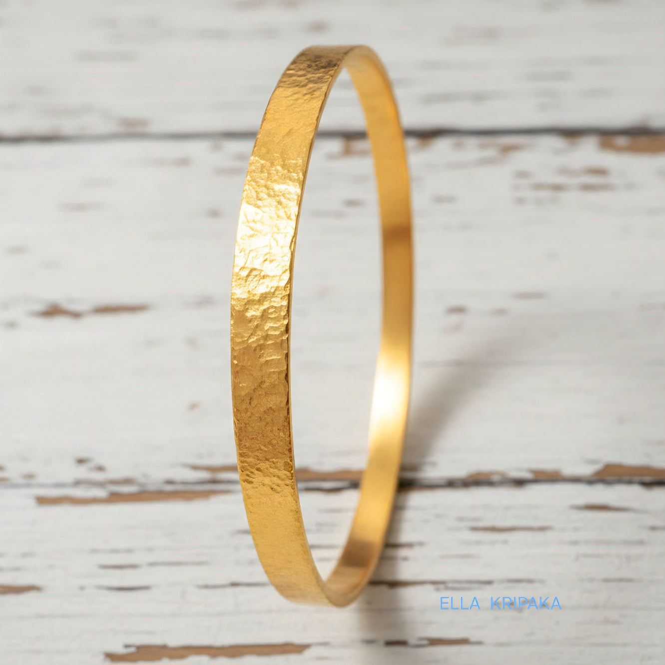 24k 9999 gold hammered Ancient Rome style bracelet bangle on white rustic wooden surface, indicating it is a custom-made jewelry with creator's name 'Ella Kripaka'
