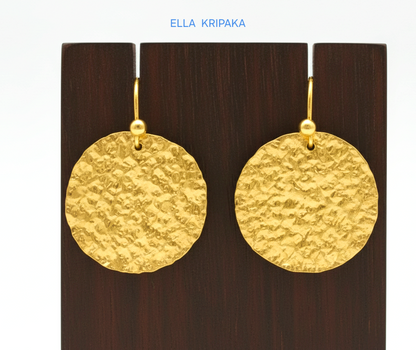Organic 24k 9999 gold hammered disk earrings with  uneven edges are on dark wooden stand and on grey background, artist-jeweler's name 'Ella Kripaka'