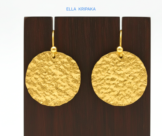 Organic 24k 9999 gold hammered disk earrings with  uneven edges are on dark wooden stand and on grey background, artist-jeweler's name 'Ella Kripaka'