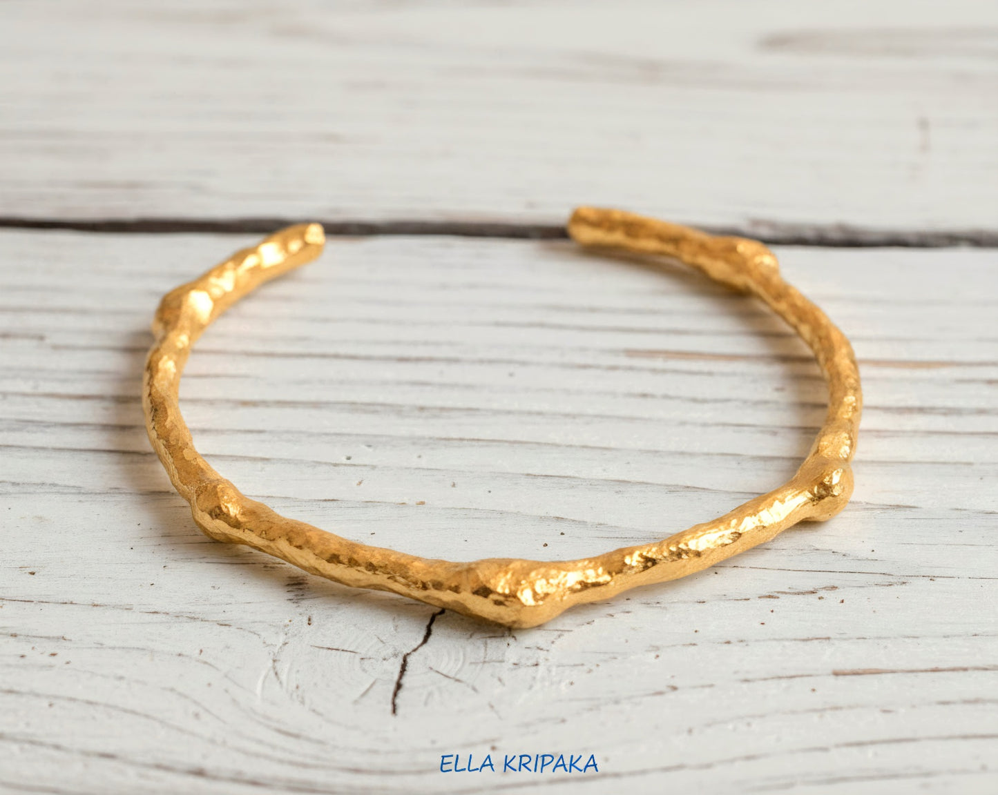 Organic hammered 24k 9999 gold bracelet uneven cuff on a old white wooden background, branding artist-jeweler name 'Ella Kripaka'