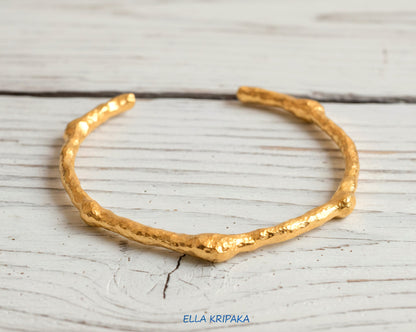 Organic hammered 24k 9999 gold bracelet uneven cuff on a old white wooden background, branding artist-jeweler name 'Ella Kripaka'