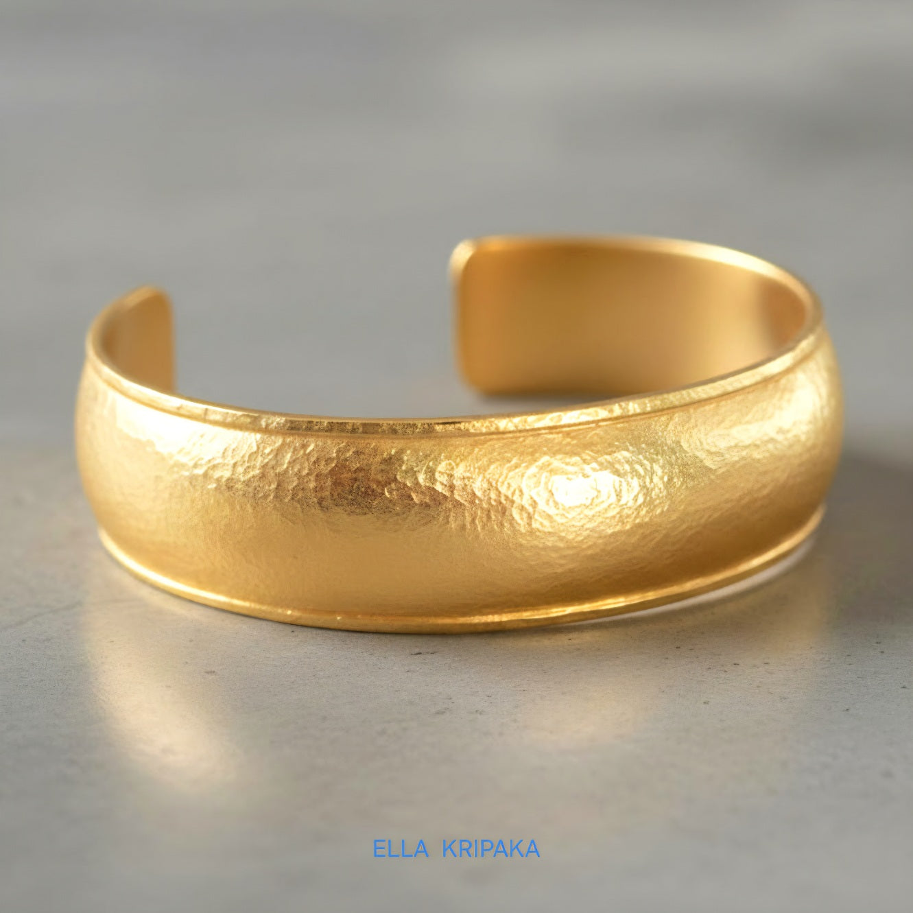 24k 9999 gold hammered Ancient Rome convex  cuff bracelet on a grey concrete surface, branded 'Ella Kripaka'