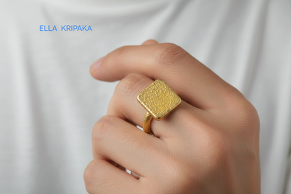 Hammered 24k 9999 Gold thick ring square signet Ancient Rome style with a textured forged gold surface worn by a person on a finger and on a white t-shirt background, branded 'Ella Kripaka'