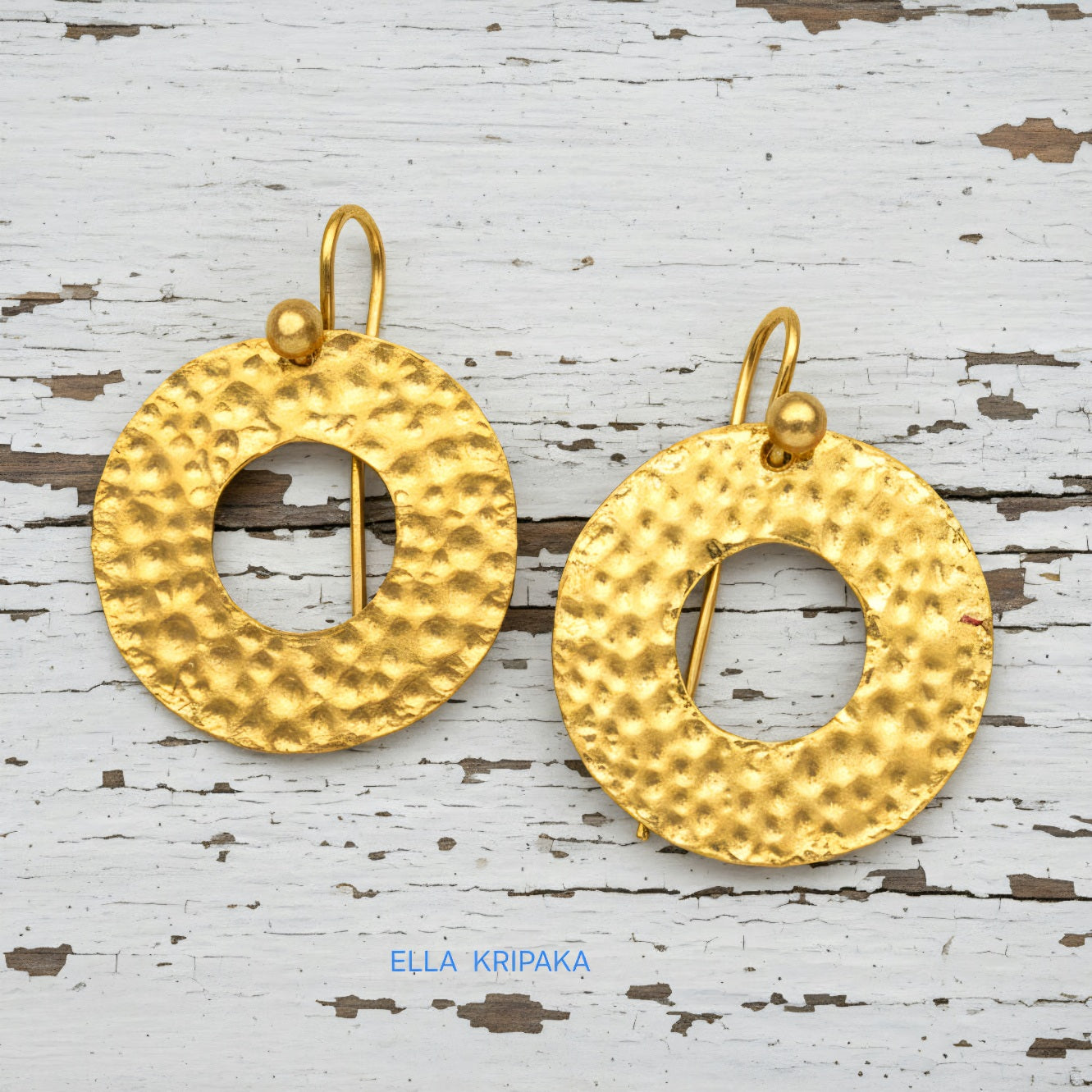 Organic 24k 9999 gold hammered hoop earrings with shiny gold textures are on white old wooden background, artist-jeweler's name 'Ella Kripaka'