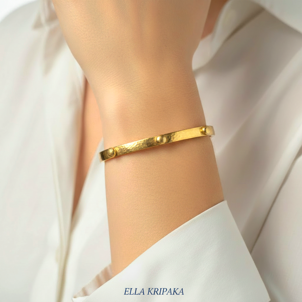 24k gold hammered cuff textured bracelet with convex rounds is worn by a woman on wrist and on white shirt background, artist 'Ella Kripaka' branding