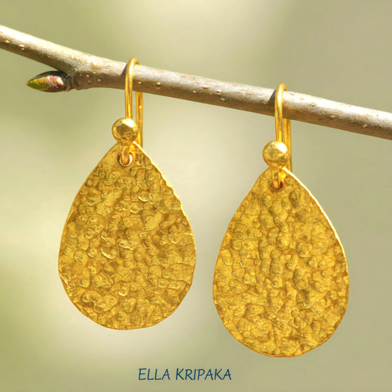 Hammered 24k gold, pure 9999 gold drop earrings with shiny forged gold textures hanging on a branch and with blurred natural background, artist-jeweler 'Ella Kripaka' branding