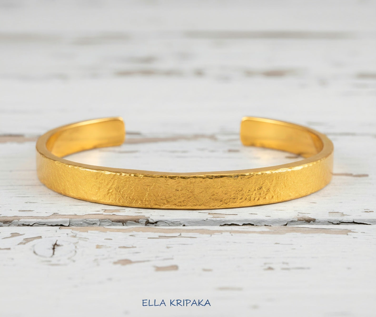 Hammered 24k 9999 gold cuff thick bracelet Ancient Rome style on old white wooden background, artist-jeweler's name 'Ella Kripaka'