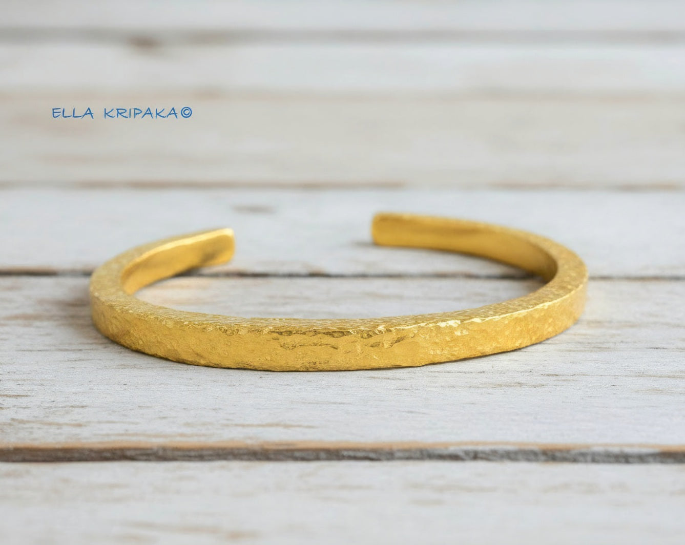 Hammered 24k 9999 gold cuff thick bracelet Ancient Rome style on an old white wooden background, artist-jeweler name 'Ella Kripaka' branding
