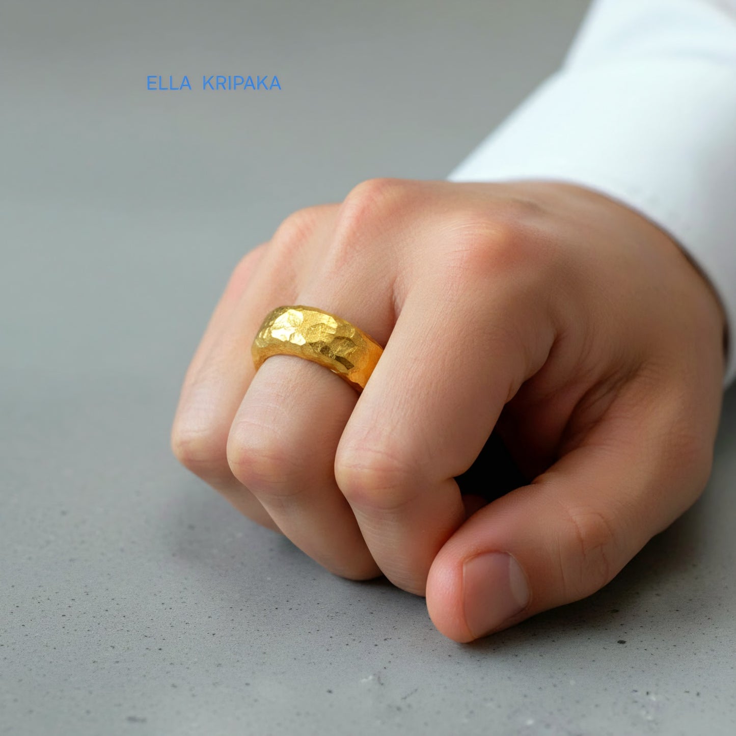 Hammered 24k 9999 Gold thick uneven ring organic with a textured gold surface worn on man's finger and on a grey background, branded 'Ella Kripaka'