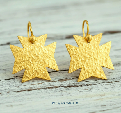 Hammered 24k gold, pure 9999 gold Byzantine cross earrings with shiny forged gold textures on white old wooden surface, artist-jeweler 'Ella Kripaka' branding