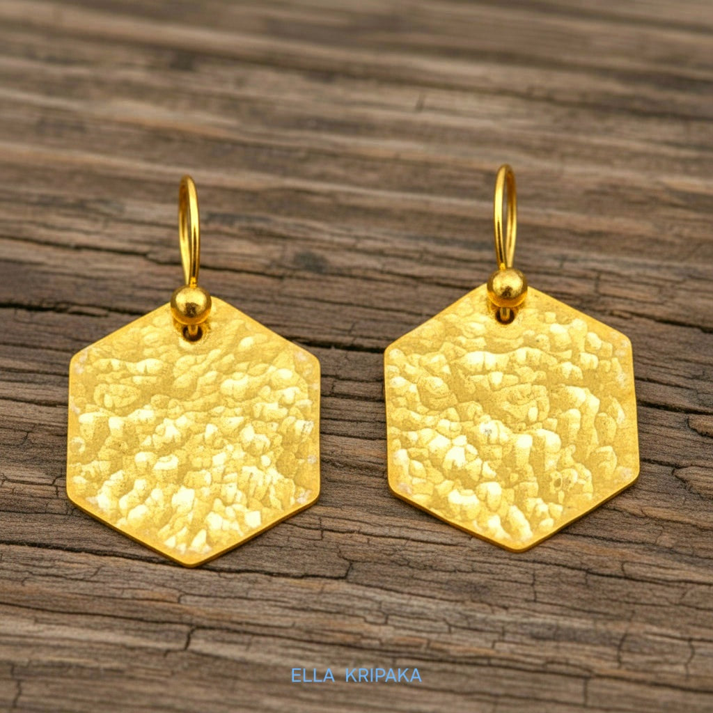 Hammered 24k gold, pure 9999 gold hexagon earrings with shiny forged gold textures on old wooden surface, artist-jeweler 'Ella Kripaka' branding