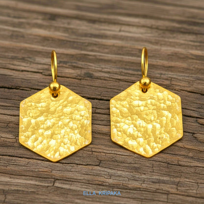 Hammered 24k gold, pure 9999 gold hexagon earrings with shiny forged gold textures on old wooden surface, artist-jeweler 'Ella Kripaka' branding