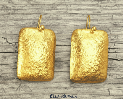 Hammered 24k gold, pure 9999 gold convex rectangular earrings with shiny forged gold textures on old wooden surface, artist-jeweler 'Ella Kripaka' branding