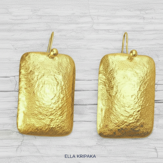 Hammered 24k gold, pure 9999 gold convex rectangular earrings with shiny forged gold textures on old wooden surface, artist-jeweler 'Ella Kripaka' branding