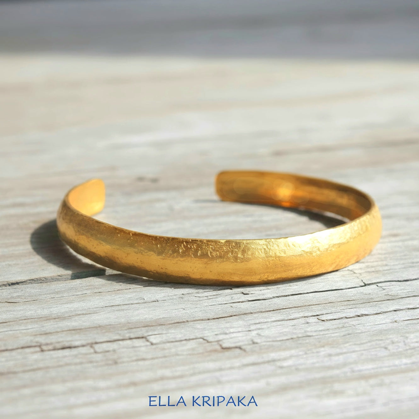 Hammered 24k gold bracelet cuff convex textured on a old light wooden background, branding artist 'Ella Kripaka'