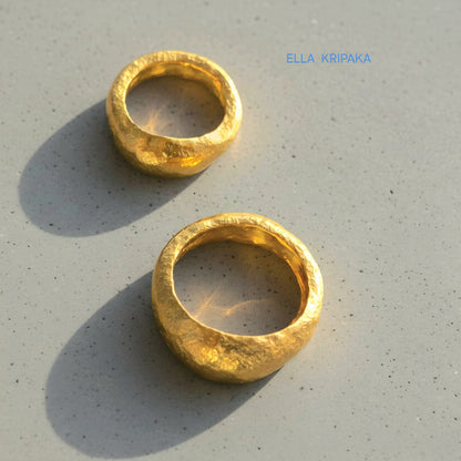 Hammered organic 24k Gold 9999 gold uneven two signets thick rings with textured gold on a grey concrete background, branded 'Ella Kripaka'