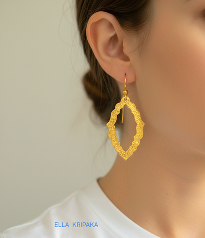 24k 9999 gold hammered Byzantine baroque convex earrings with shiny gold textures are worn by a woman and on grey background, artist-jeweler's name 'Ella Kripaka'