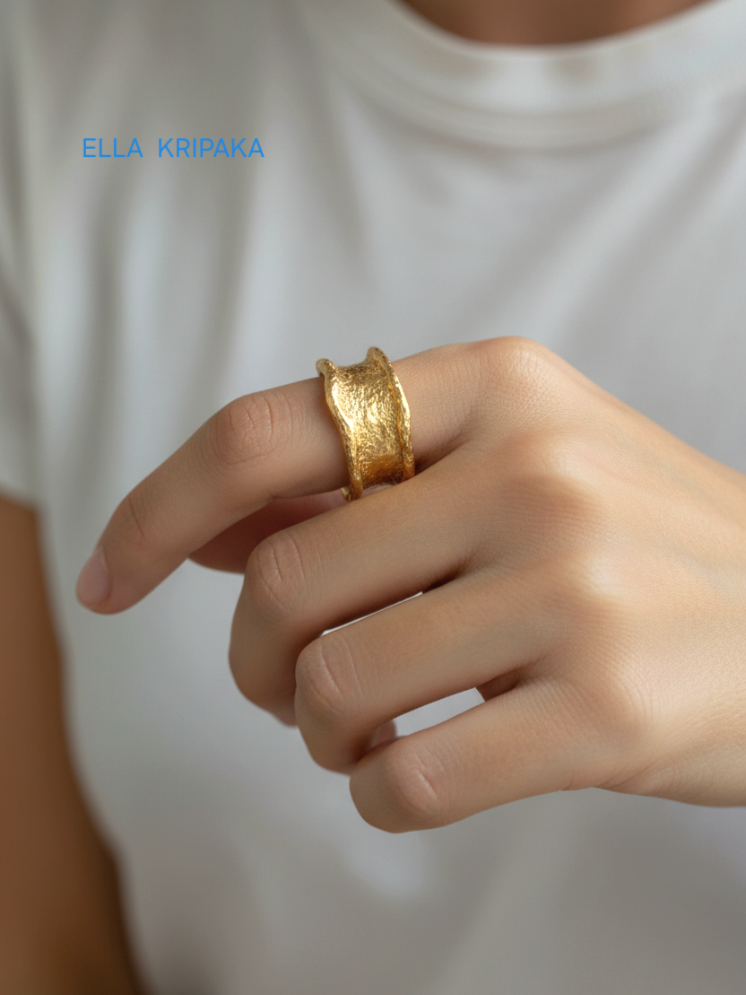 Organic 24k gold hammered ring with uneven edges and with textured surface on a woman's finger with white t-shirt background, branded 'Ella Kripaka'
