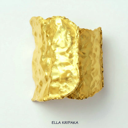 Hammered 24k gold cuff bracelet with convex uneven textures on backside and on a white paper background, and with 'Ella Kripaka' branding