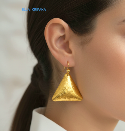 Hammered 24k gold, pure 9999 gold convex triangle earring with shiny forged gold textures worn on a woman and with light grey background, artist-jeweler 'Ella Kripaka' branding