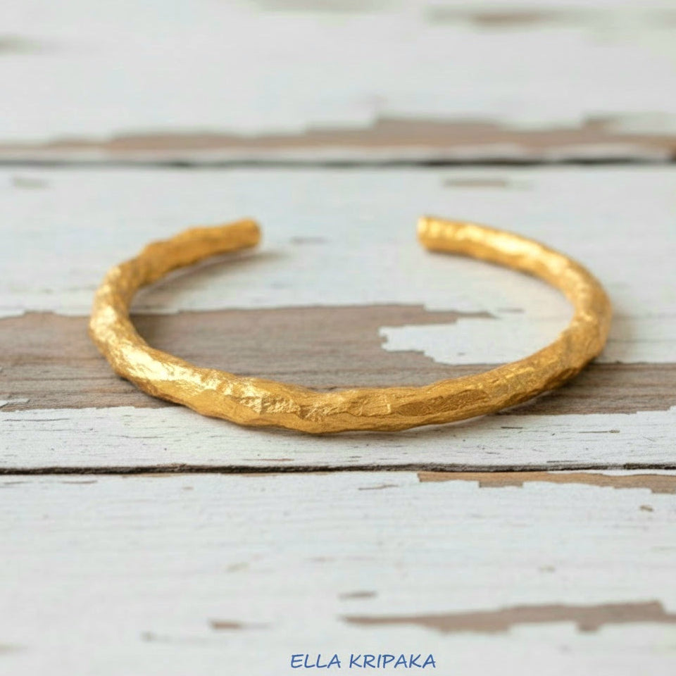 Organic hammered 24k 9999 gold bracelet uneven cuff on a old white old wooden background, branding artist-jeweler name 'Ella Kripaka'