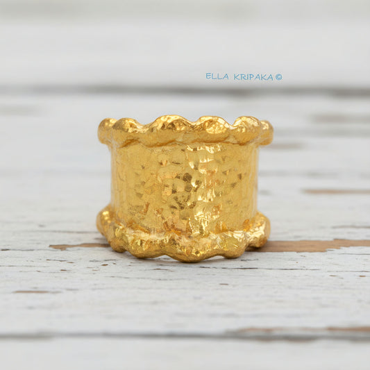 Organic hammered 24k 9999 Gold ring signet with uneven wavy thick edges on white old wooden surface, artist-jeweler's name 'Ella Kripaka' is written in picture