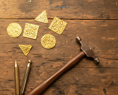 Hammered Gold jewelry pieces and jewelry tools and jewelry hammer on old rustic wooden surface with artist's name 'Ella Kripaka' branding