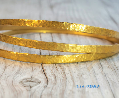Hammered 22k gold three textured bangles bracelets Ancient Rome style on old wooden surface with 'Ella Kripaka' branding