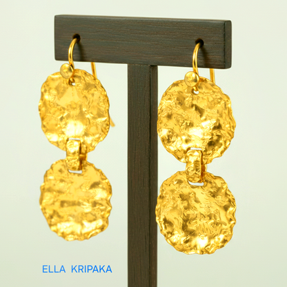 Organic hammered 24k gold earrings wavy disks with uneven edges on a dark wooden stand and on light grey background with artist's name 'Ella Kripaka' branding