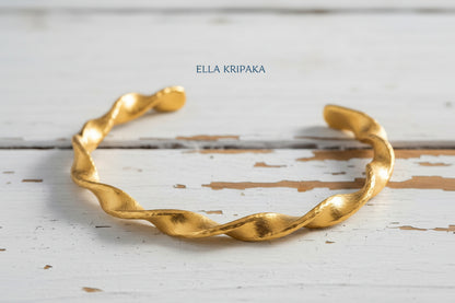 Twisted Viking hammered 24k 9999 gold bracelet cuff on a old white old wooden background, branding artist-jeweler name 'Ella Kripaka'