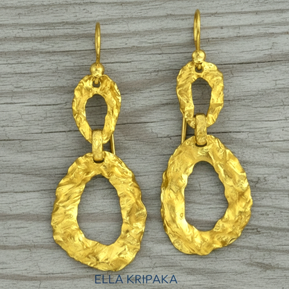 Organic hammered uneven 24k 9999 Gold earrings on a grey wooden surface, and with 'ELLA KRIPAKA' branding