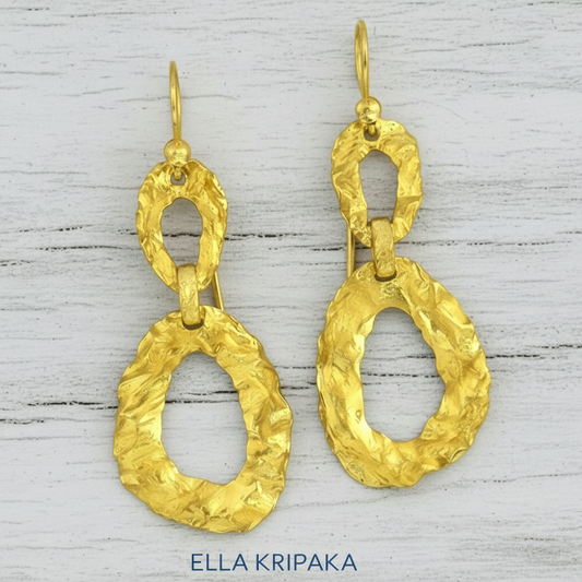 Organic hammered uneven 2 ovals hoops 24k Gold earrings with wavy textures on a white rusic wooden surface, and with 'ELLA KRIPAKA' branding