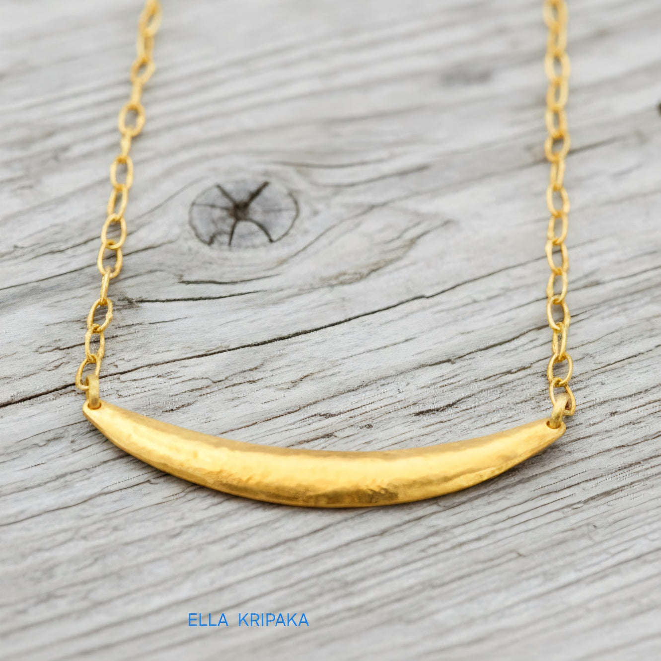 Hammered 24k gold convex Moon pendant with chain on a grey rustic wooden background with 'Ella Kripaka' branding