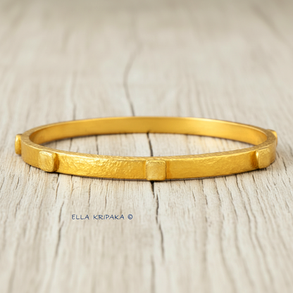 24k gold hammered bangle textured bracelet with thick squares on white rustic wooden surface, artist 'Ella Kripaka' branding