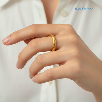 Organic 24k gold hammered ring with uneven textured surface on a person's finger with white shirt blurred background, branded 'Ella Kripaka'
