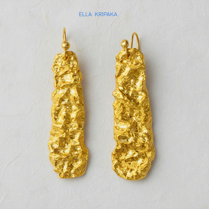 Organic hammered uneven 24k 9999 Gold earrings on a light grey surface, and with 'ELLA KRIPAKA' branding.