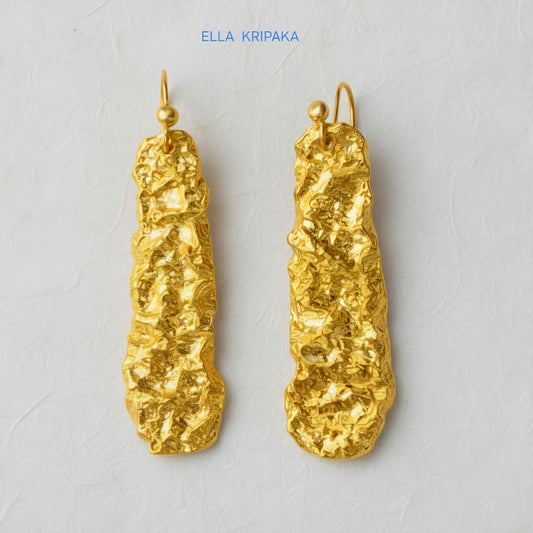Organic hammered uneven 24k 9999 Gold earrings on a light grey surface, and with 'ELLA KRIPAKA' branding.