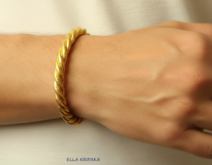 Twisted Viking Hammered 24k gold bracelet thick cuff 'rope style' with a textured gold on person's wrist on blurred white backgroud, branded artist 'Ella Kripaka'