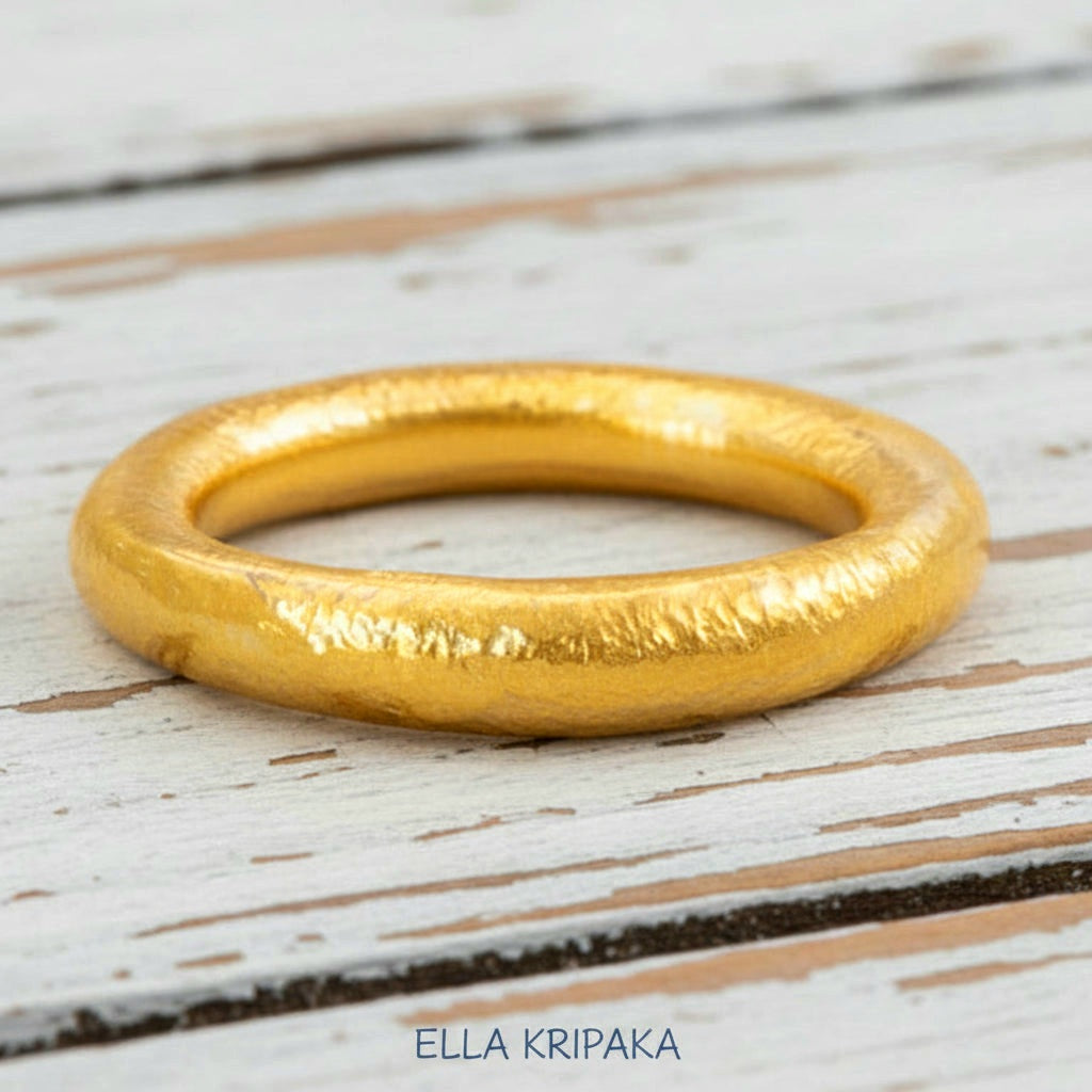 Hammered 24k gold rounded textured ring on a white rustic wooden surface with 'Ella Kripaka' branding.