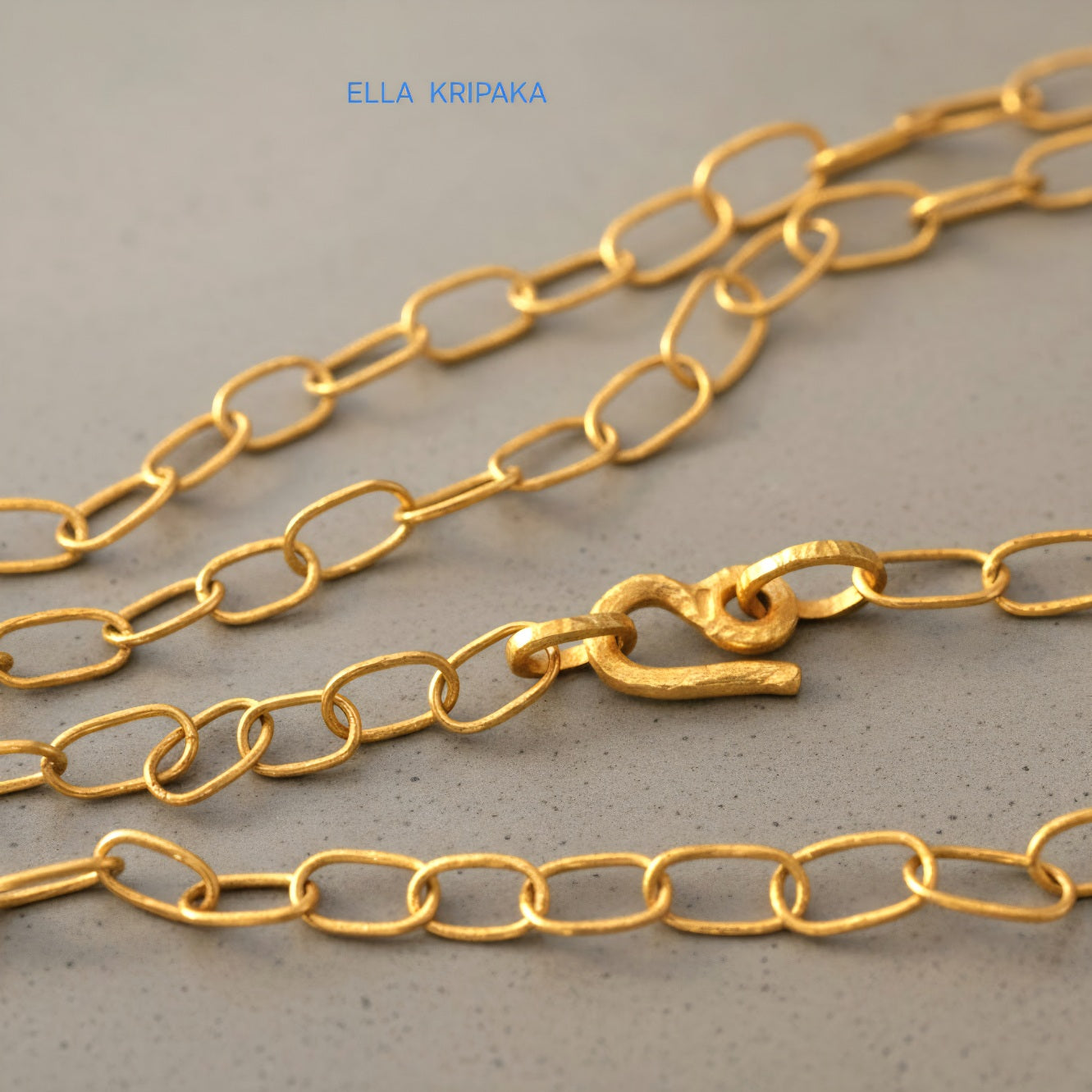 22k gold hammered chain necklace with thick hook clasp on grey concrete background, artist-jeweler's name 'Ella Kripaka' branding