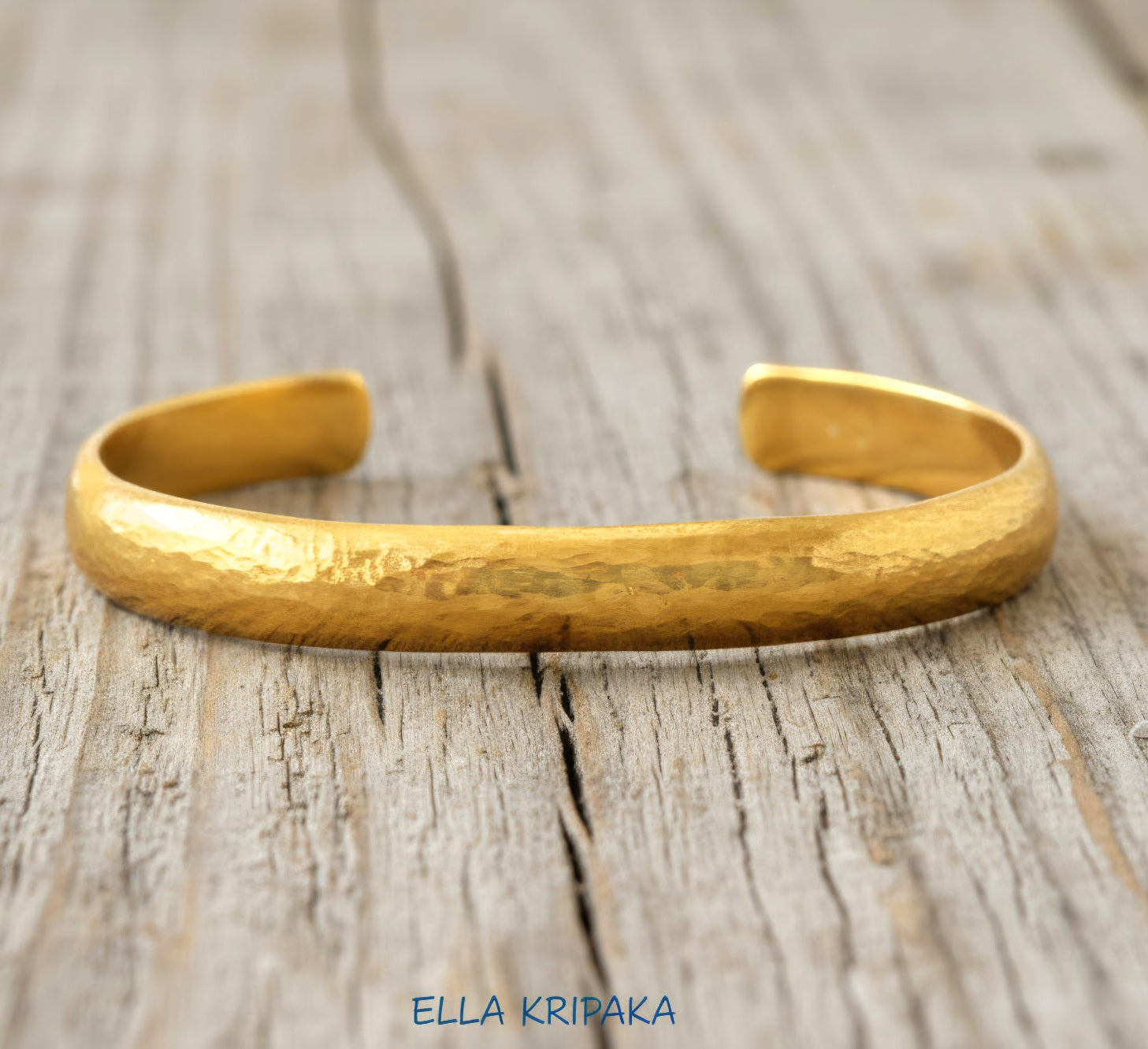 Hammered 24k gold bracelet cuff convex textured on a rustic light wooden background, branding artist 'Ella Kripaka'