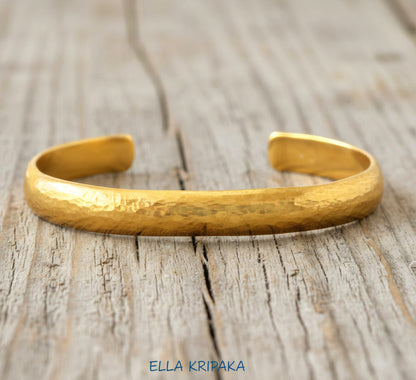 Hammered 24k gold bracelet cuff convex textured on a rustic light wooden background, branding artist 'Ella Kripaka'